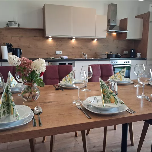 An inviting dining area with a wooden table that is beautifully set. In the background, you can see a modern kitchen.