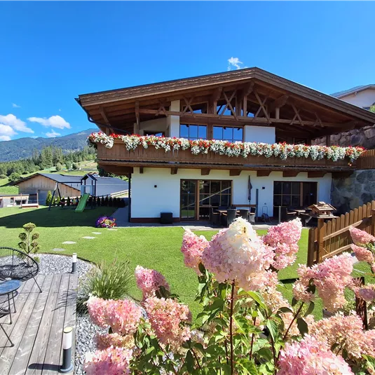 A beautiful house with wooden cladding and floral decoration. In the foreground, pink hydrangeas are blooming in a well-kept garden.