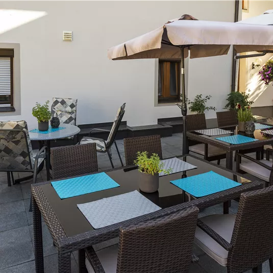 A cozy terrace with several tables and chairs. Umbrellas provide shade and plants create an inviting atmosphere.