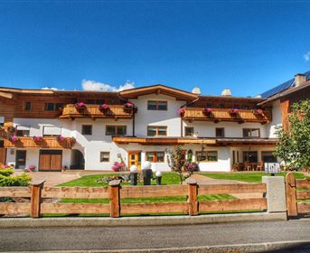 Ein gemütliches Haus mit traditionellen Balkonen und schöner Gartenanlage. Der Himmel ist blau und die Umgebung ist malerisch.