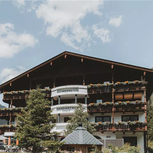 Ein charmantes Hotel in den Bergen mit einem traditionellen alpinen Design. Umgeben von Bäumen und Bergen, strahlt es eine gemütliche Atmosphäre aus.