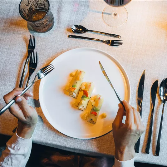 Ein schön angerichteter Teller mit Teigtaschen und Gemüse. Im Hintergrund sind elegante Bestecke und Gläser zu sehen.
