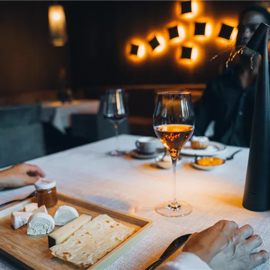 Ein elegantes Restaurant mit gedeckten Tischen. Auf dem Tisch sieht man eine Käseplatte, ein Glas Wein und eine ansprechende Atmosphäre.