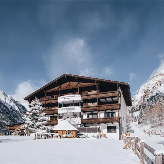 Ein gemütliches Gebäude im Winter mit schneebedecktem Boden. Die umliegenden Berge sind teilweise mit Schnee bedeckt und der Himmel ist klar.