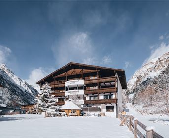 Ein gemütliches Gebäude im Winter mit schneebedecktem Boden. Die umliegenden Berge sind teilweise mit Schnee bedeckt und der Himmel ist klar.