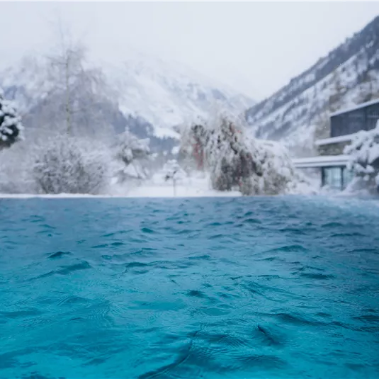 Ein wunderschöner, blauer Pool in einer verschneiten Berglandschaft. Die ruhige Winteratmosphäre lädt zum Entspannen ein.