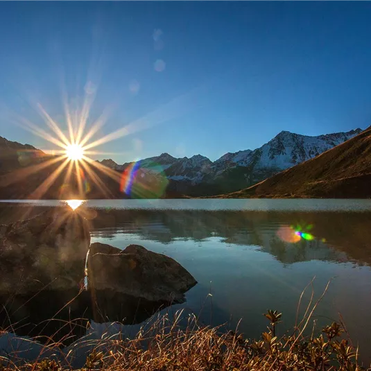 A sunny morning at the lake with mountains in the background. The sun shines over the calm water, creating sparkling reflections.