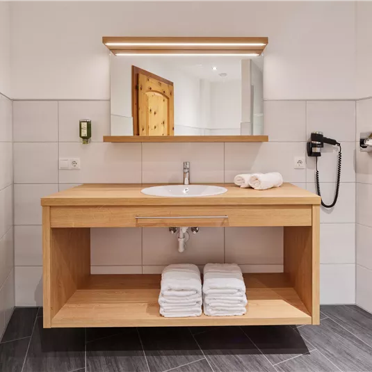 A modern bathroom with a wooden washbasin and a large mirror. Clean towels are neatly stacked underneath.