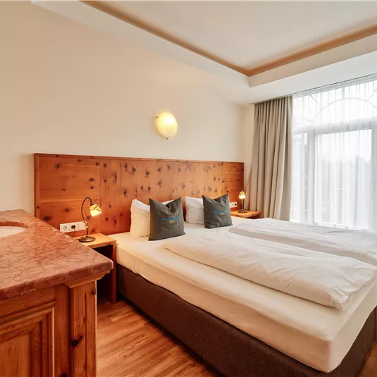 A cozy bedroom with a large double bed and wood paneling. Bright curtains let in plenty of daylight.