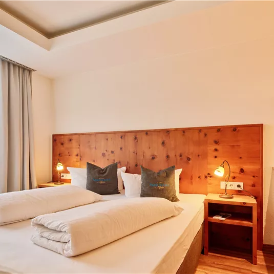 A cozy hotel room with two beds and a wooden panel. Large windows provide plenty of daylight.