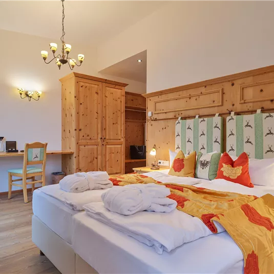A bright and cozy room with wooden paneling and modern amenities. The bed is invitingly decorated and there is a view of a television and a desk.