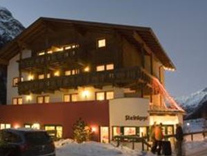 Ein gemütliches Hotel in den Bergen, umgeben von Schnee. Die warmen Lichter des Gebäudes strahlen in der Abenddämmerung.