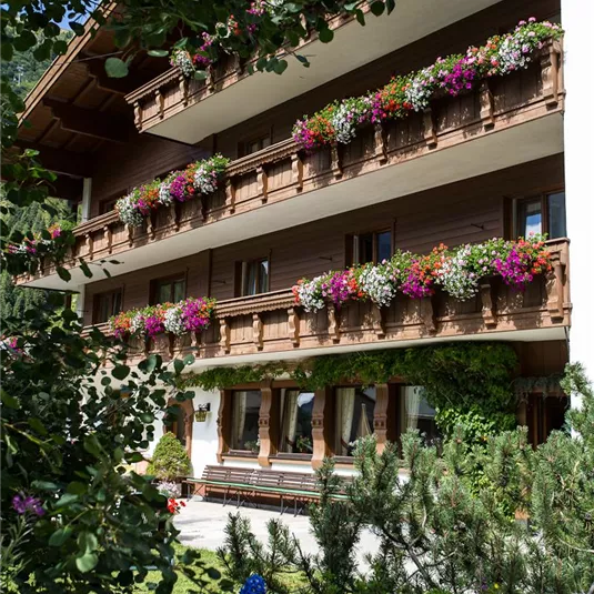 Ein charmantes Gebäude mit Blumenkästen an den Balkonen. Umgeben von gepflegtem Grün und bunten Blumen.