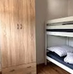 A simple bedroom with a bunk bed and a wardrobe. The floor is made of wood and a rug is on the floor.