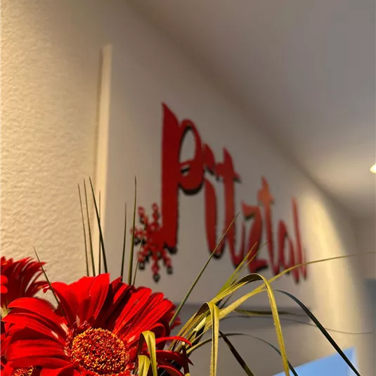 A decorative sign with the word "Putzial" on the wall. In the foreground, bright red flowers are visible.