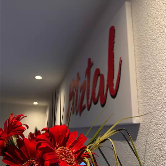 A friendly entrance area with a color panel that says "Pitztal." Red flowers give the room a vibrant accent.