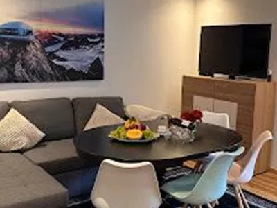 A modern living room with a gray couch and a round dining table. On the table are fresh fruit and a beautiful floral decoration.