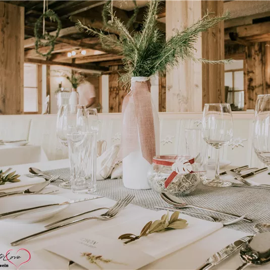 Ein liebevoll gedeckter Tisch in einem gemütlichen Restaurant. Die Dekoration besteht aus einem Vase mit Pflanzen und elegantem Geschirr.