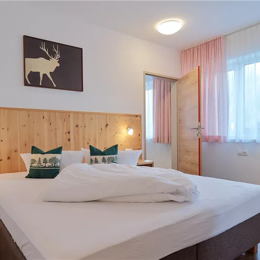 A modern bedroom with a large bed and wooden details. The large windows provide plenty of daylight and a cozy atmosphere.