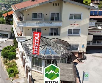 Ein charmantes Gebäude im Pitztal mit einer gläsernen Veranda und einem großen roten Banner. Das Hotel bietet eine attraktive Aussicht auf die umliegende Berglandschaft.