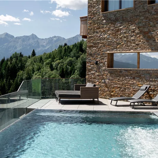 Ein moderner Pool mit Blick auf die Berge und grüne Wälder. Entspannte Liegen laden zum Verweilen ein.