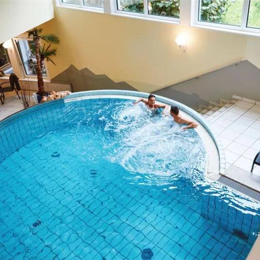 Ein rundes Schwimmbecken in einem modernen Raum. Zwei Personen schwimmen und spritzen im Wasser.