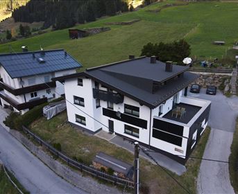 A modern building with a black and white facade, surrounded by green meadows. In the background, mountainous landscapes are visible.