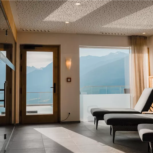 Ein eleganter Raum mit Liegen und großen Fenstern, die einen Blick auf die Berge bieten. Das Licht schafft eine entspannende Atmosphäre.