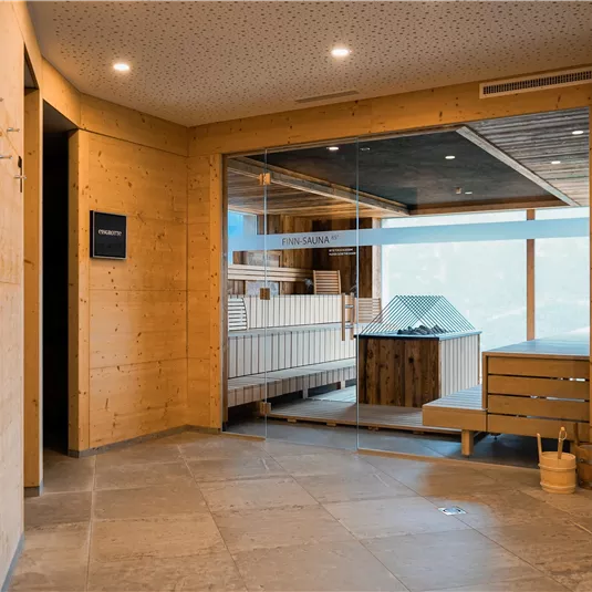 Ein modernes Zimmer mit Holzverkleidung und großen Fenstern. Im Hintergrund ist ein Wellnessbereich mit Sauna zu sehen.