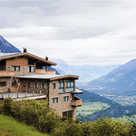 Ein modernes Gebäude in den Bergen mit einer schönen Aussicht auf das Tal. Der Himmel ist bewölkt und die Landschaft ist grün.