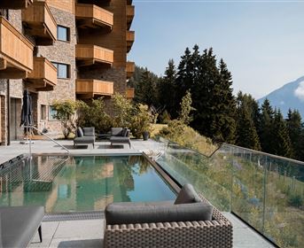 A modern terrace with a pool and comfortable seating. In the background, mountains and forests are visible, creating a relaxed atmosphere.