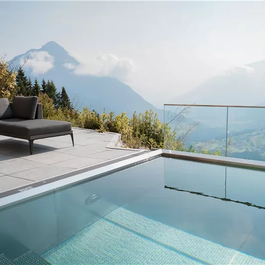 Ein eleganter Außenbereich mit einem Pool und modernen Liegen. Im Hintergrund sind atemberaubende Berge und eine ruhige Landschaft zu sehen.