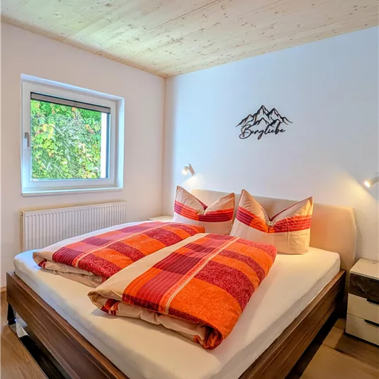 A cozy bedroom with a large double bed. The window offers a view of the greenery.