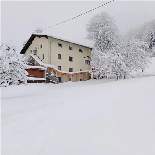 A snow-covered landscape with a cozy building. The trees are also covered in snow, and the sky is gray and overcast.