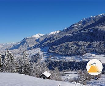 Eine malerische Winterlandschaft mit schneebedeckten Bergen und Bäumen. Der klare blaue Himmel ergänzt die ruhige, friedliche Atmosphäre.