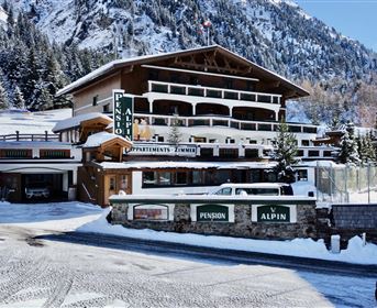 Ein charmantes Hotel in einer schneebedeckten Berglandschaft. Umgeben von Bäumen und Bergen bietet es eine gemütliche Atmosphäre.