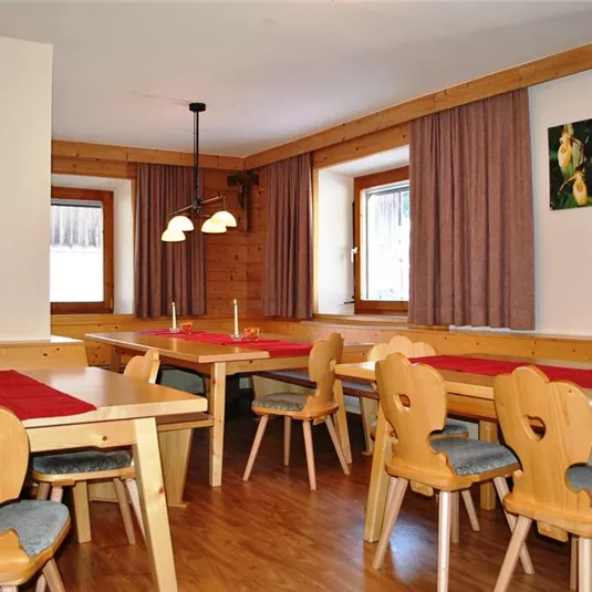 A cozy dining area with wooden tables and chairs. The walls are adorned with curtains and artwork.