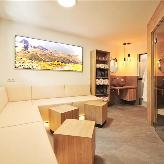 Ein modernes Wellnesszimmer mit einer gemütlichen Sitzecke und Holzdetails. An der Wand ist ein großes Bild einer Berglandschaft zu sehen.