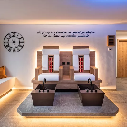 A modern wellness room with two massage chairs and a water basin. Soft lighting and a relaxing ambiance create a calm atmosphere.