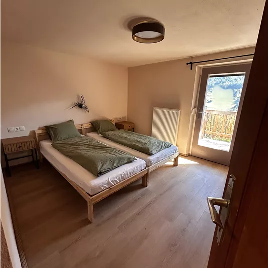 A cozy room with two single beds and light blankets. The room has plenty of natural light and access to a balcony.