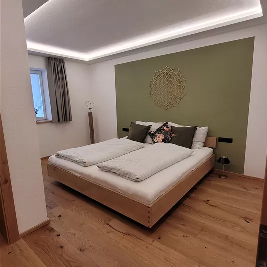 Ein modernes Schlafzimmer mit einem großen Doppelbett und Holzfußboden. Die Wände sind in sanften Farben gehalten und es gibt sanftes Licht von der Decke.