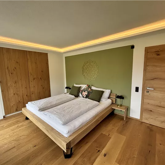 Ein modernes Schlafzimmer mit einem Doppelbett und stilvollen Kissen. Die Wände sind in sanften Farben gehalten und der Boden ist aus Holz.