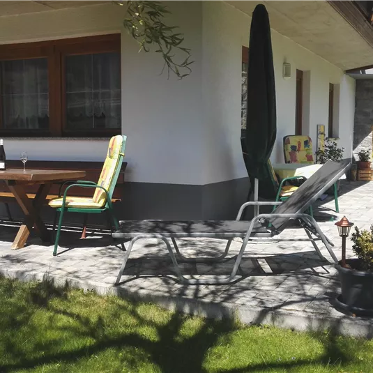 A cozy terrace with a table and chairs. In the background, a sunny garden with a well-maintained lawn can be seen.