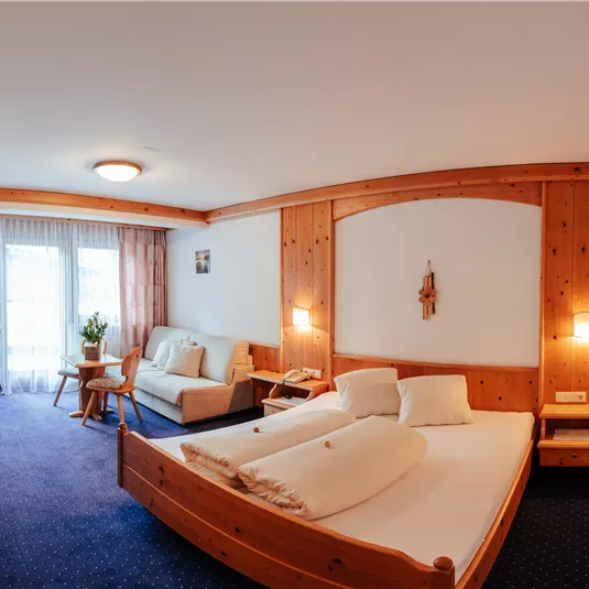 A cozy hotel room with wooden decor and two beds. There is a seating area and large windows that provide plenty of light.