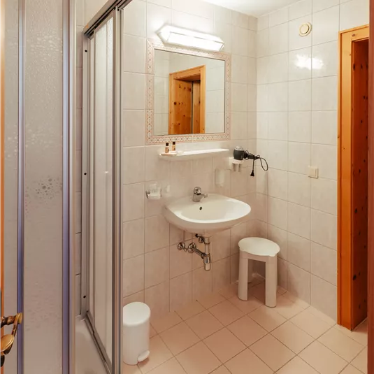 A modern bathroom with light tiles, a shower, and a sink. The room has pleasant lighting and a minimalist style.