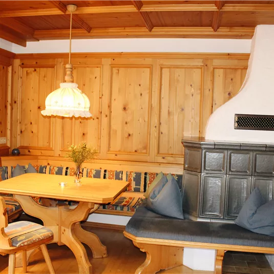 A cozy room with wooden paneling and a rustic table. A bench with colorful cushions invites you to linger.