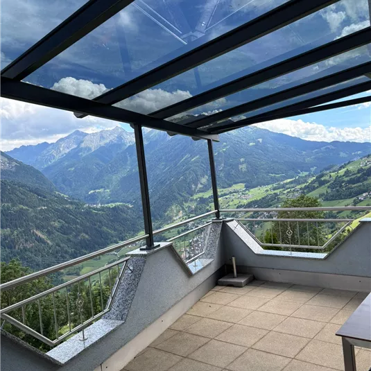 Eine moderne Terrasse mit Glasdach und Blick auf die Berge. Die Landschaft ist grün und beeindruckend.