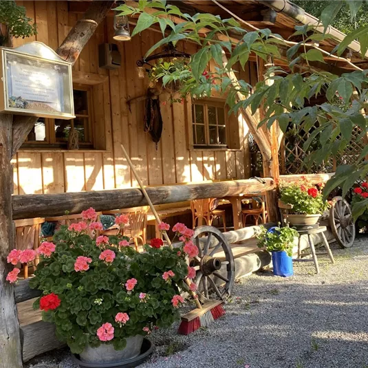 A cozy wooden house with colorful flowers and plants in the foreground. The atmosphere is welcoming and rural.