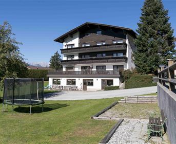 A large building with several floors, surrounded by a green garden. Nearby is a trampoline and a relaxed environment with trees.