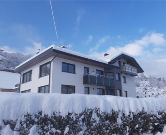 Ein modernes Haus in einer verschneiten Landschaft. Der Himmel ist klar und blau, während der Schnee die Umgebung bedeckt.